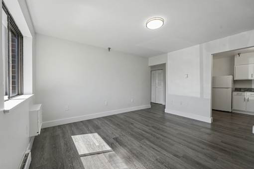 A room with a window on the left and a wooden floor.