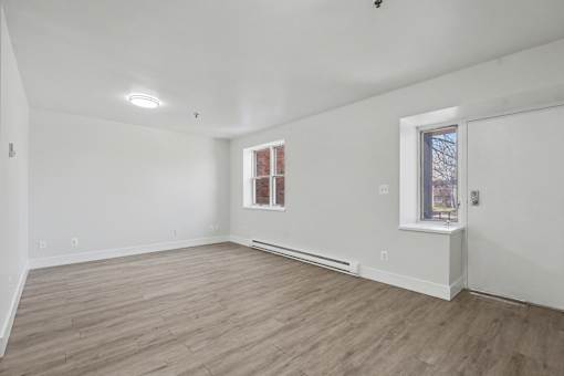 A room with wooden flooring and two windows.