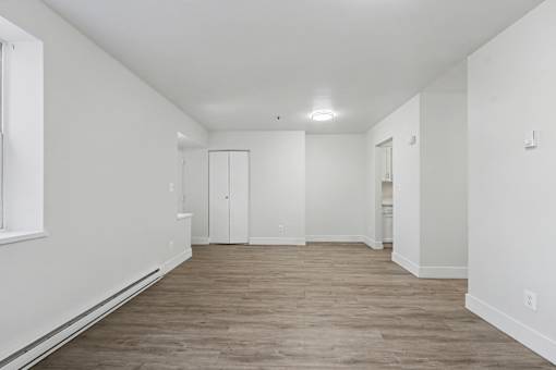 A large empty room with wood flooring and white walls.