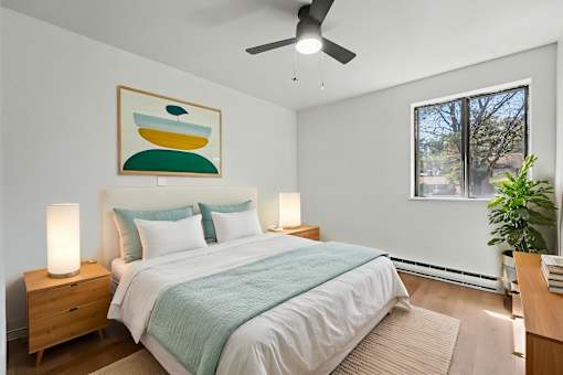 A bedroom with a bed, a ceiling fan, and a painting on the wall.