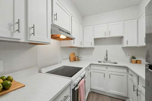 A kitchen with white cabinets and a cutting board with green apples on it.