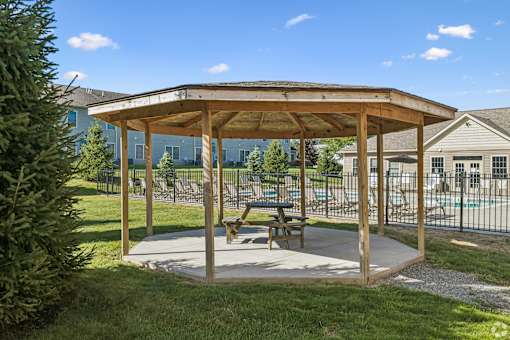 A wooden pavilion with a picnic table sits in a grassy area.