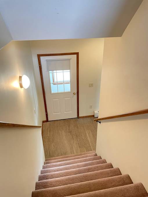 A staircase with a brown carpeted runner and white walls.