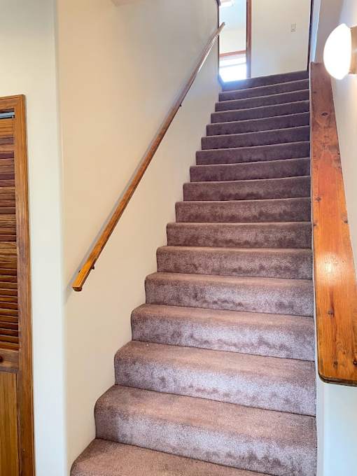 A staircase with a wooden handrail and beige carpeted steps.
