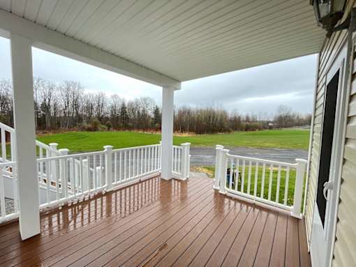 A wooden deck with a white railing and a view of a field.