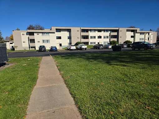 A concrete pathway leads to a parking lot in front of a building.