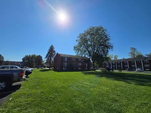 A sunny day at a grassy parking lot with cars and a building in the background.