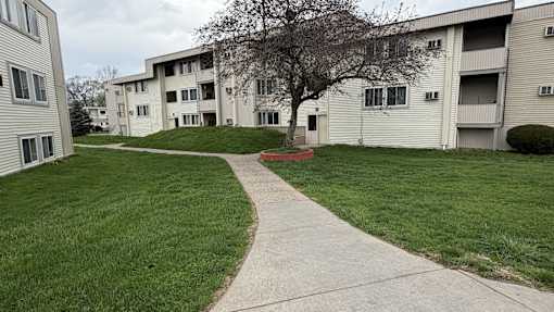 A grassy area in front of apartment buildings with a concrete walkway.