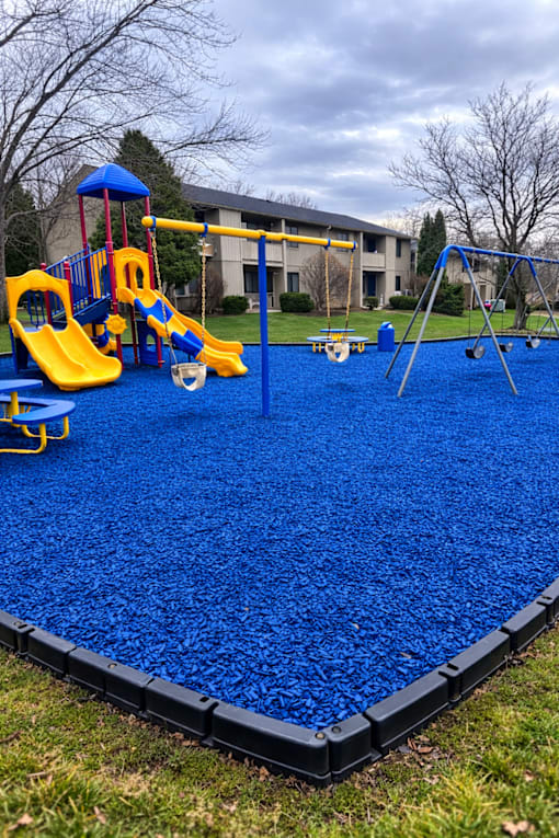 A playground with a blue rubberized surface and yellow slides.