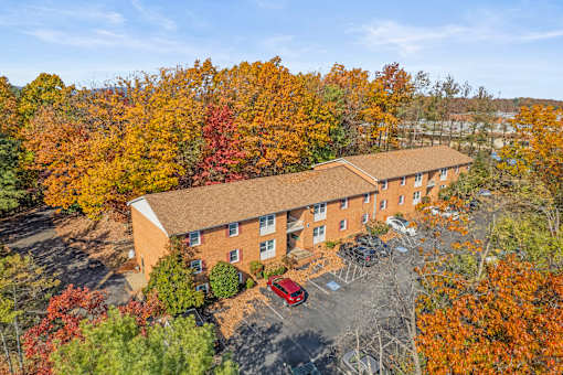 An aerial view of a red car parked in front of a brick building surrounded by trees with autumn foliage.