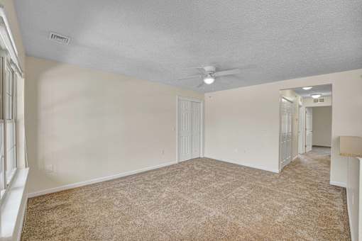 A spacious room with a carpeted floor and a ceiling fan.