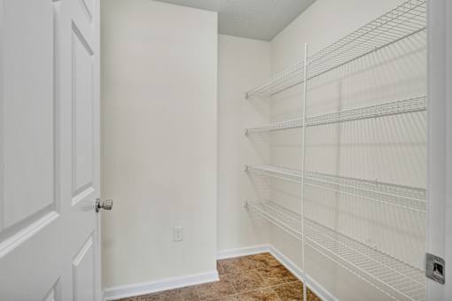 A white door is open to a room with a white wall and a white shelving unit.
