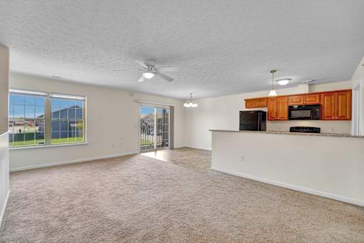 A spacious living room with a ceiling fan and a kitchenette.