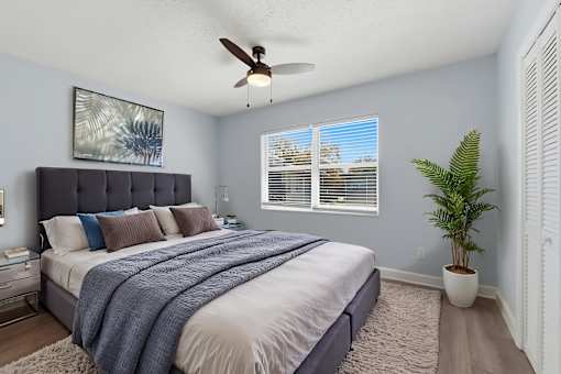 A bedroom with a bed, a ceiling fan, and a potted plant.