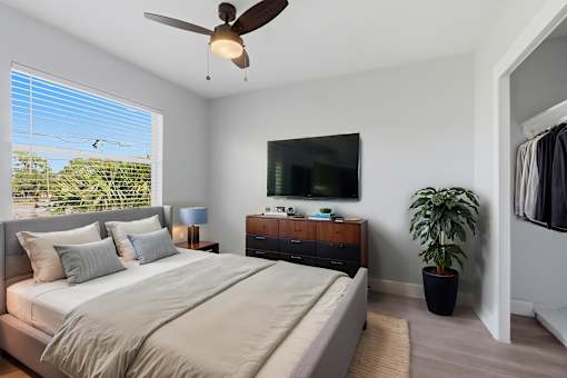 A bedroom with a large bed, a ceiling fan, and a flat-screen TV mounted on the wall.