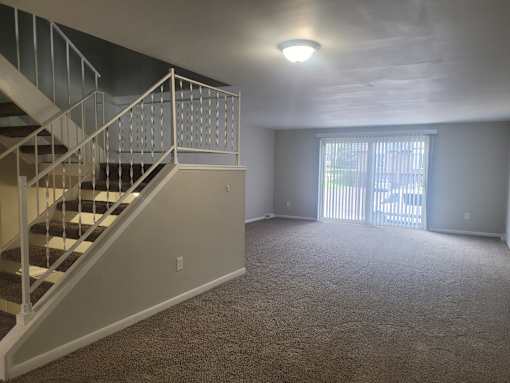 A carpeted room with a staircase and a window.