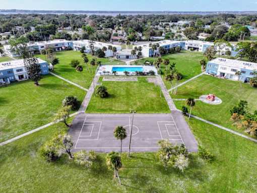 A tennis court is surrounded by a grassy area and a pool.