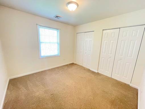 A room with a carpeted floor, a window, and a ceiling light.
