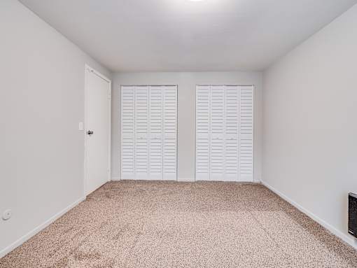 A room with white walls and a carpeted floor with two closets.
