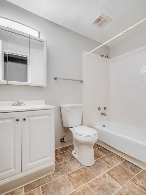 A white toilet sits in a bathroom next to a sink and a bathtub.