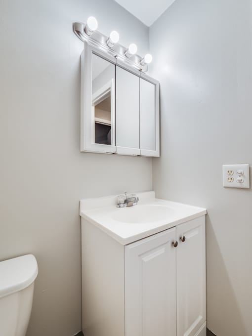 A white bathroom with a sink, mirror, and toilet.