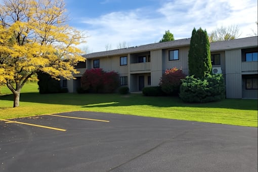 A parking lot in front of a building with trees and bushes.