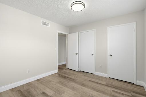 Three white doors in a room with wood flooring and white walls.