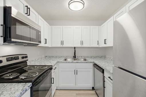 A kitchen with white cabinets and a marble countertop.