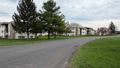 A road in front of apartment buildings with trees on the side.
