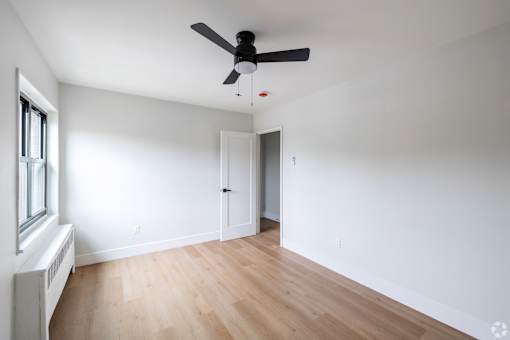 A room with a ceiling fan and a window with a radiator.