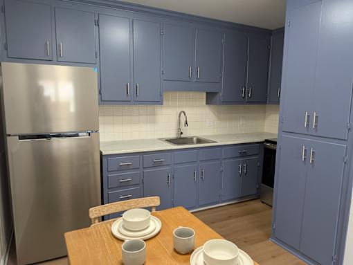 A kitchen with blue cabinets and a stainless steel refrigerator.