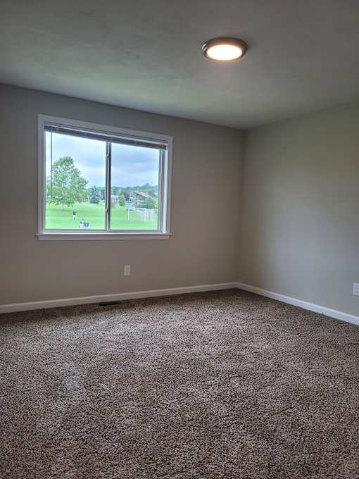 A room with a carpeted floor and a window overlooking a green field.