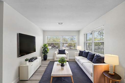 A living room with a white couch, a wooden coffee table, and a flat-screen TV mounted on the wall.