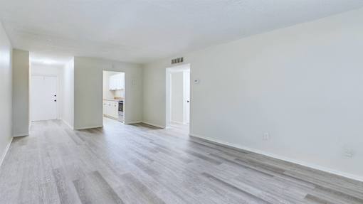 A spacious room with wood flooring and white walls.