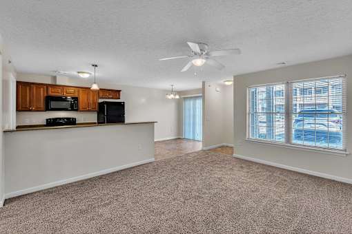 an empty living room with a kitchen and a ceiling fan