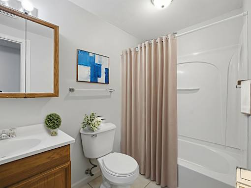 A bathroom with a white toilet, a sink, a shower, and a painting on the wall.