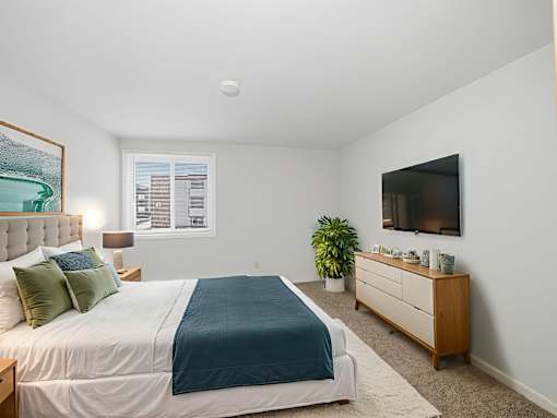 A bedroom with a bed, nightstand, and a plant.