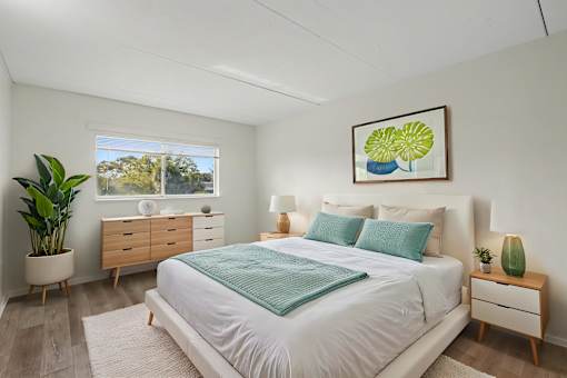 A bedroom with a large bed, a dresser, and a potted plant.