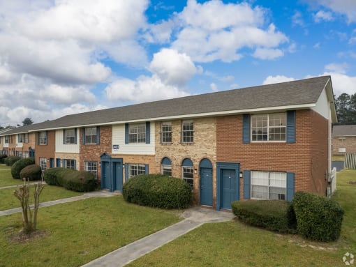 a brick apartment building with blue doors and a grass yard