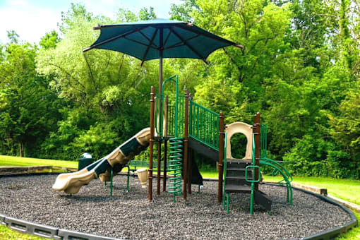 A playground with a green umbrella and a slide.