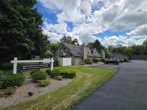 A sign for Brookside East Apartments is in front of a house.