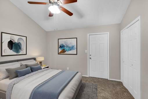 A bedroom with a bed, a ceiling fan, and two paintings on the wall.