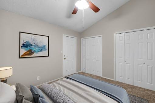 A bedroom with a bed, a ceiling fan, and a painting on the wall.