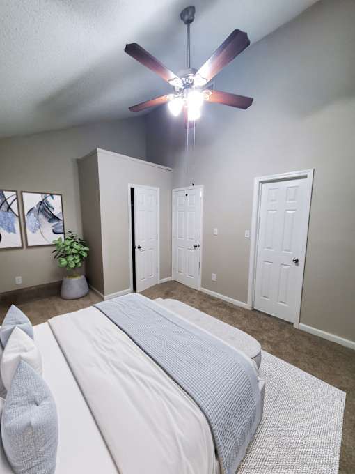 A bedroom with a bed, a ceiling fan, and a plant.