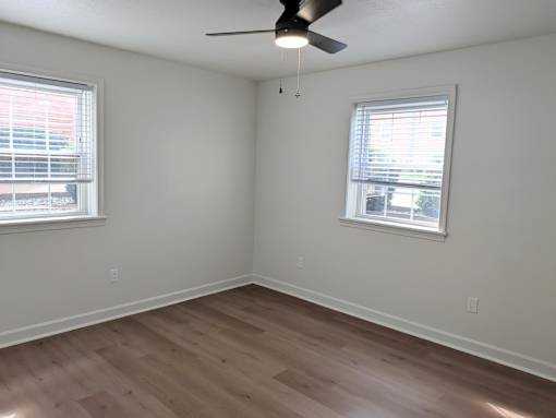 A room with a ceiling fan and two windows.