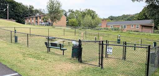 A black fence surrounds a green trash can and bench.