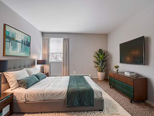A bedroom with a bed, nightstand, and a plant.