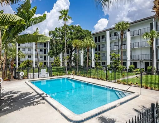 A pool in front of a white building surrounded by trees.