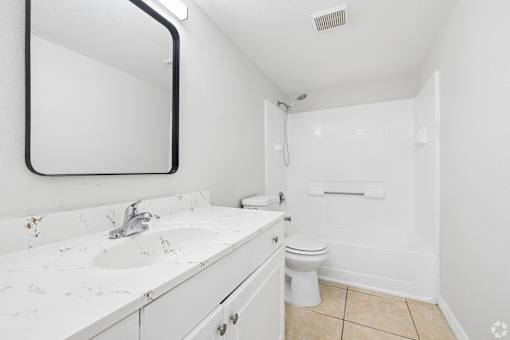 A white bathroom with a sink, mirror, and toilet.