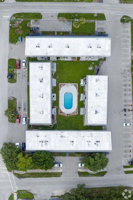 A swimming pool is located in the middle of a grassy area surrounded by buildings.